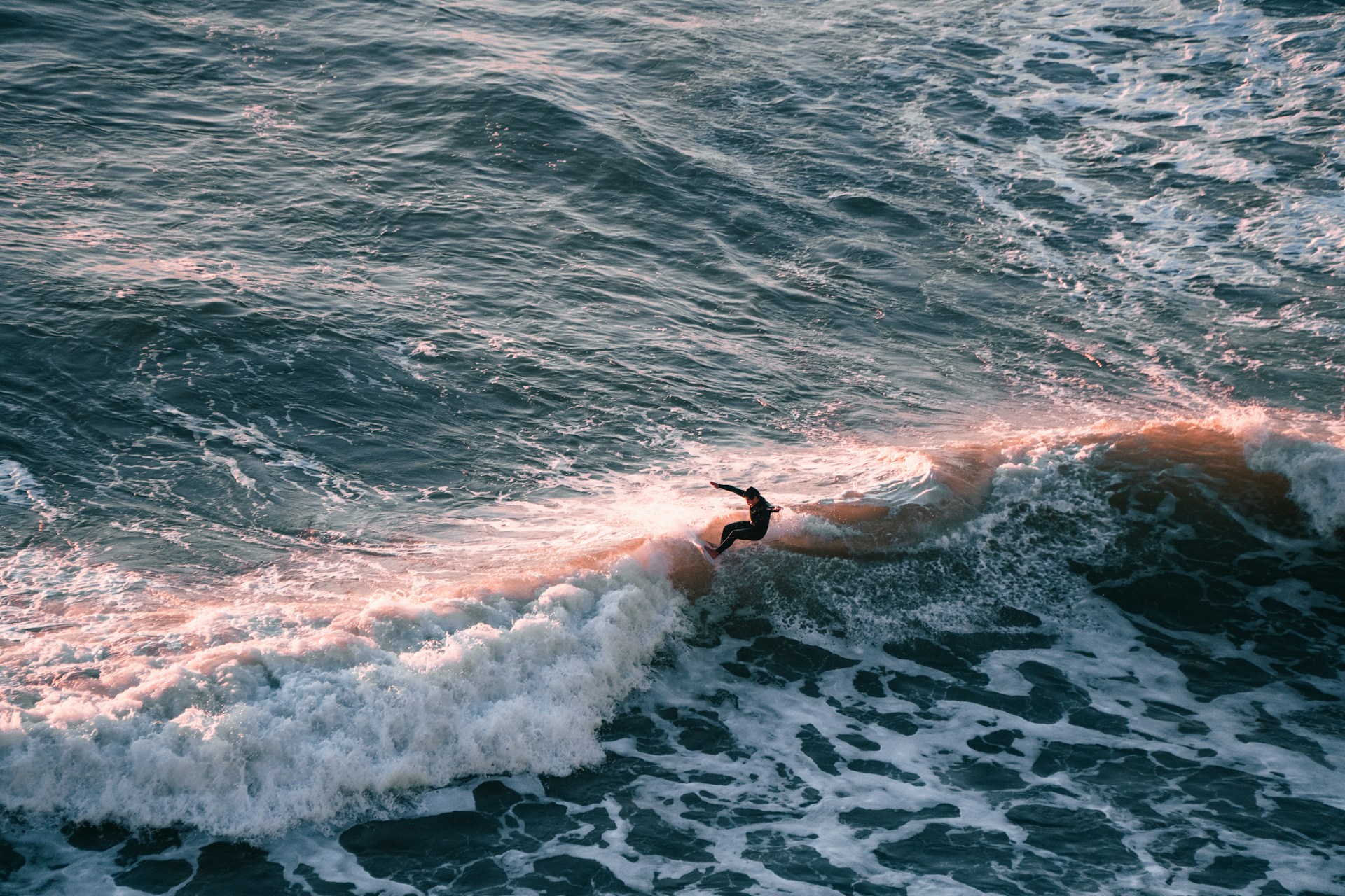 A vibrant shot of a surfer catching a wave at sunrise, wearing Bright Eye's signature relaxed-fit hoodie and board shorts.