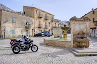 A cobblestone street in a quaint European village with a motorcycle leaning against a wall.