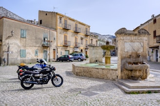 A cobblestone street in a quaint European village with a motorcycle leaning against a wall.