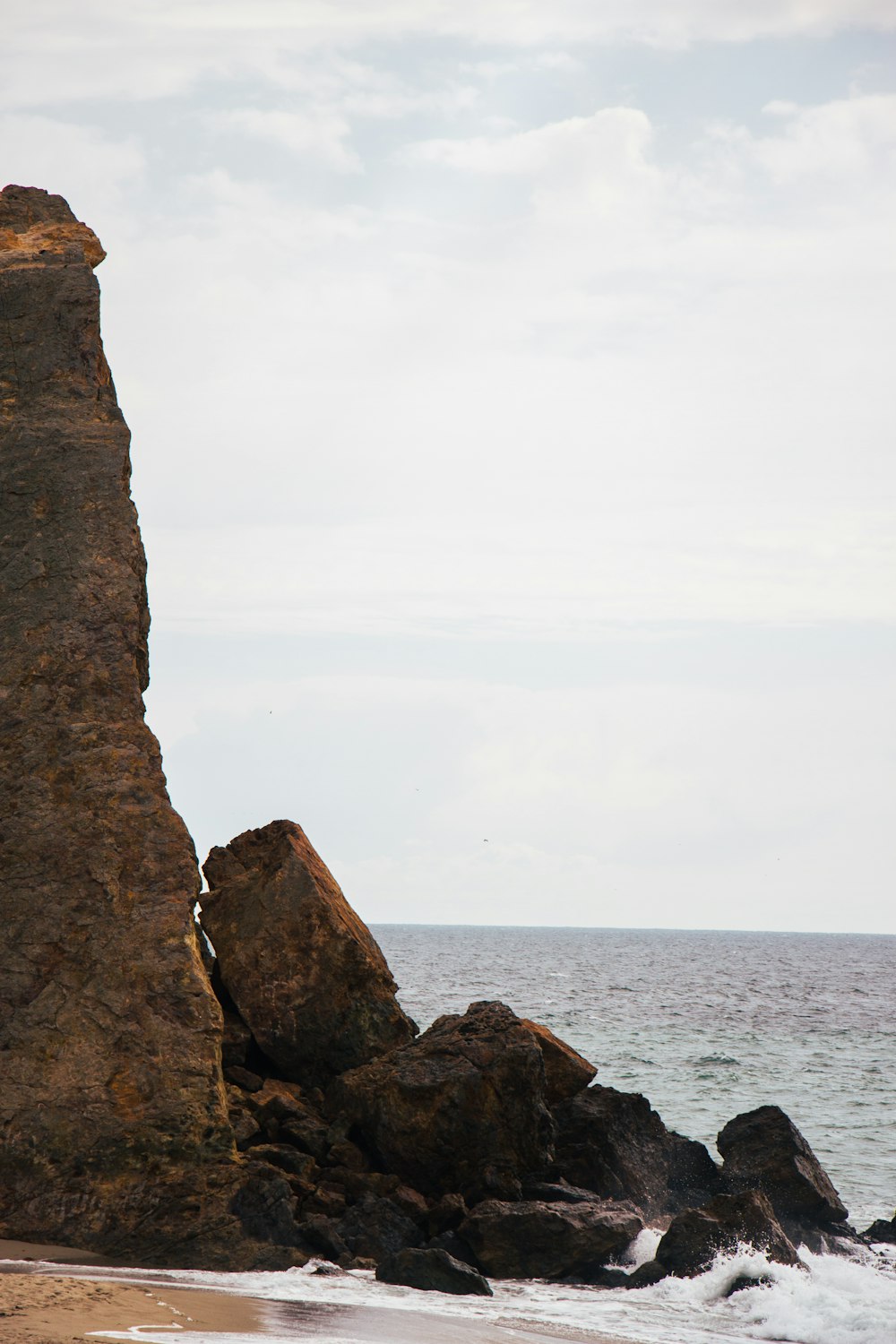 a large rock sticking out of the ocean next to a beach