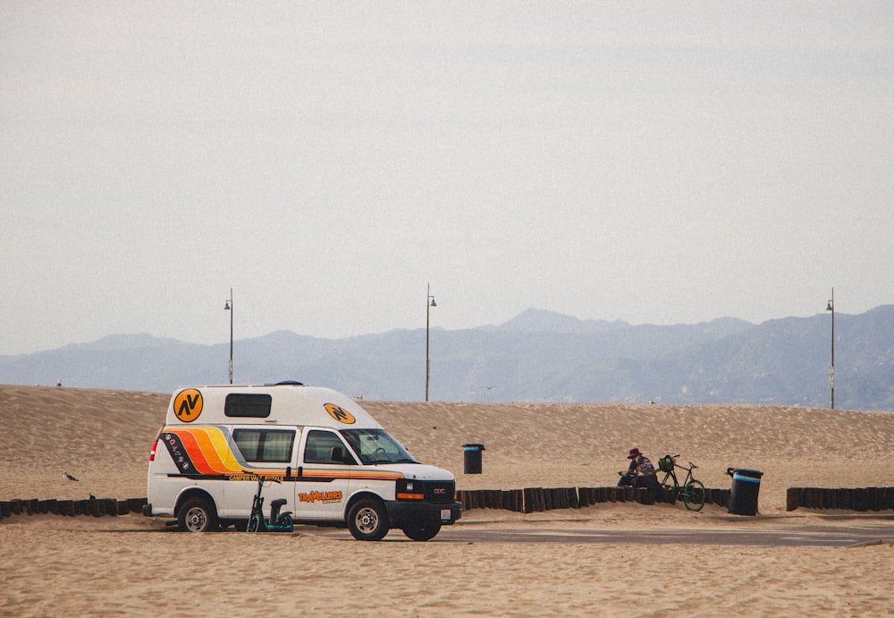 a van parked in the sand near a bike