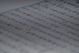 A close-up of a page containing text written in both blue and red ink. The characters appear to be of East Asian origin, possibly Japanese or Chinese. The focus is on the central area of the page, with some blurring at the edges. Red ink highlights certain words or symbols throughout the text.