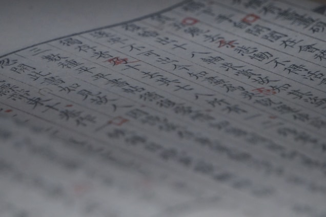 A close-up of a page containing text written in both blue and red ink. The characters appear to be of East Asian origin, possibly Japanese or Chinese. The focus is on the central area of the page, with some blurring at the edges. Red ink highlights certain words or symbols throughout the text.