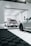 A modern garage space with sleek, luxury cars. One car is parked inside the garage, while another is partially visible in the foreground, showcasing its stylish rims. The area is well-lit, featuring a clean, minimalistic design with a predominantly white and black color scheme.