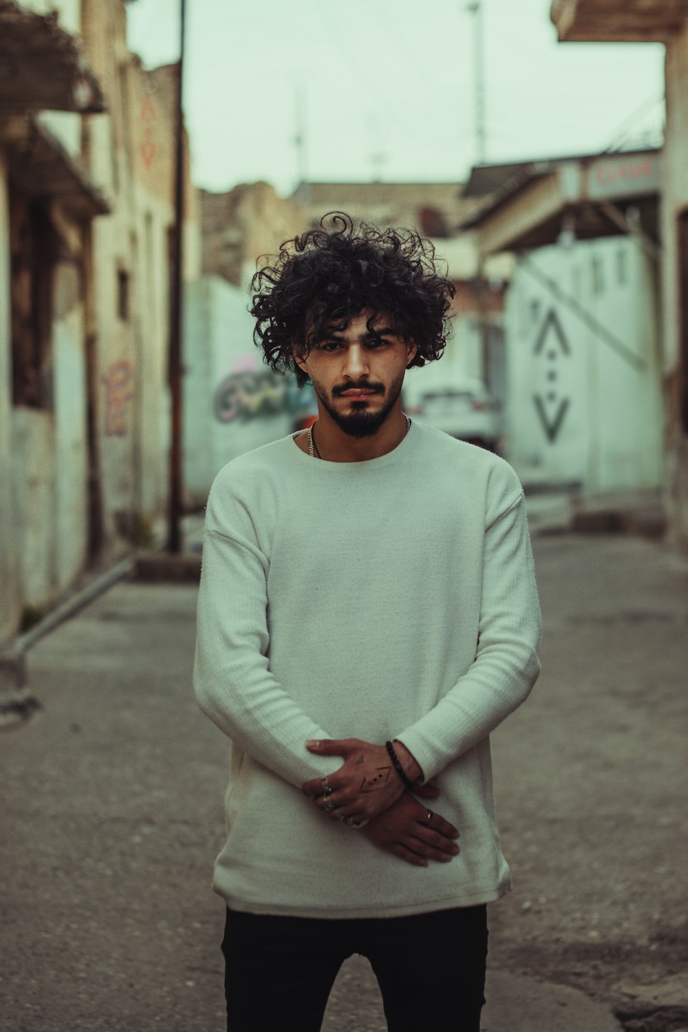 a man with curly hair standing in an alley