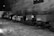 A series of mining carts line up in an underground cavern with rough, textured walls. The carts appear slightly weathered and are situated on icy or snowy ground. Some informational signs are attached to them.