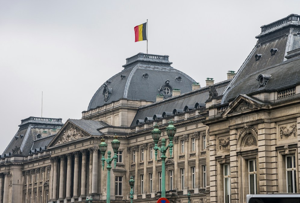 La façade du Palais royal de Bruxelles, surmontée du drapeau belge, sous un ciel gris
