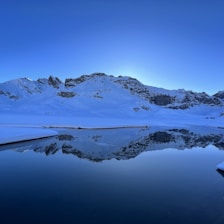 A breathtaking 4K shot of snow-capped mountains reflected perfectly in a still, dark lake at dawn.