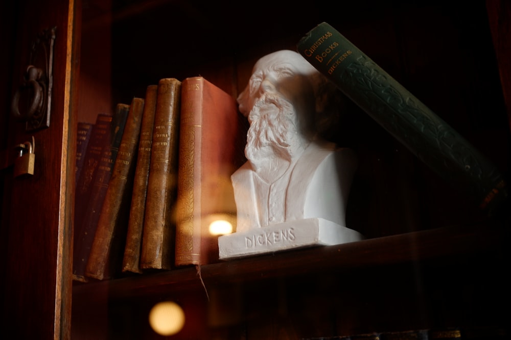 a busturine of a man with a book on a shelf