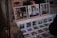 A display of art prints and photographs featuring urban and graffiti-covered scenes is set up on a table. Larger framed images rest on wooden stands, while a series of smaller prints are laid out before them. There are also visible stacks of prints to the side. Behind the display, a person holding a sandwich is partially visible.