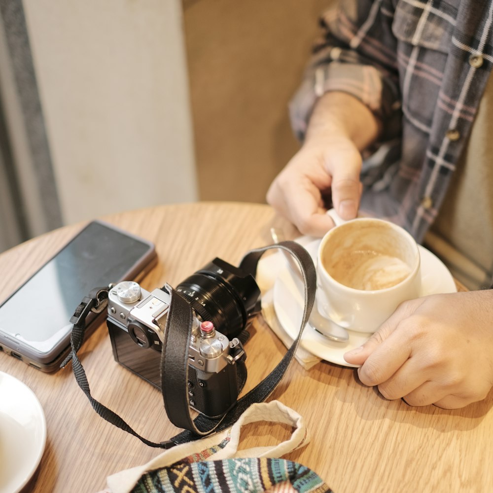 uma pessoa sentada em uma mesa com uma câmera e uma xícara de café