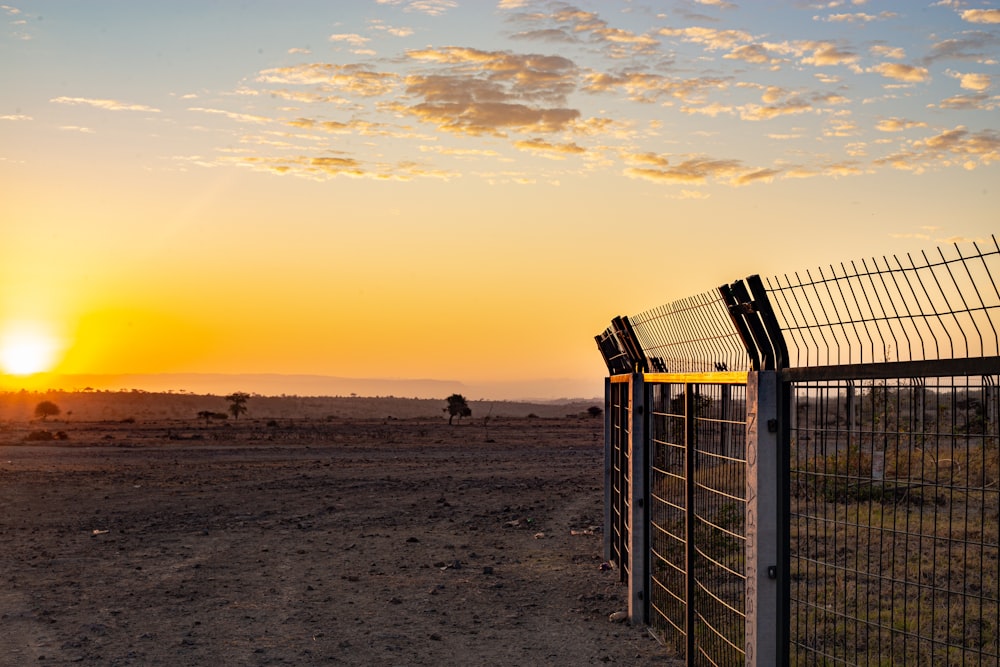 the sun is setting behind a fence in the desert