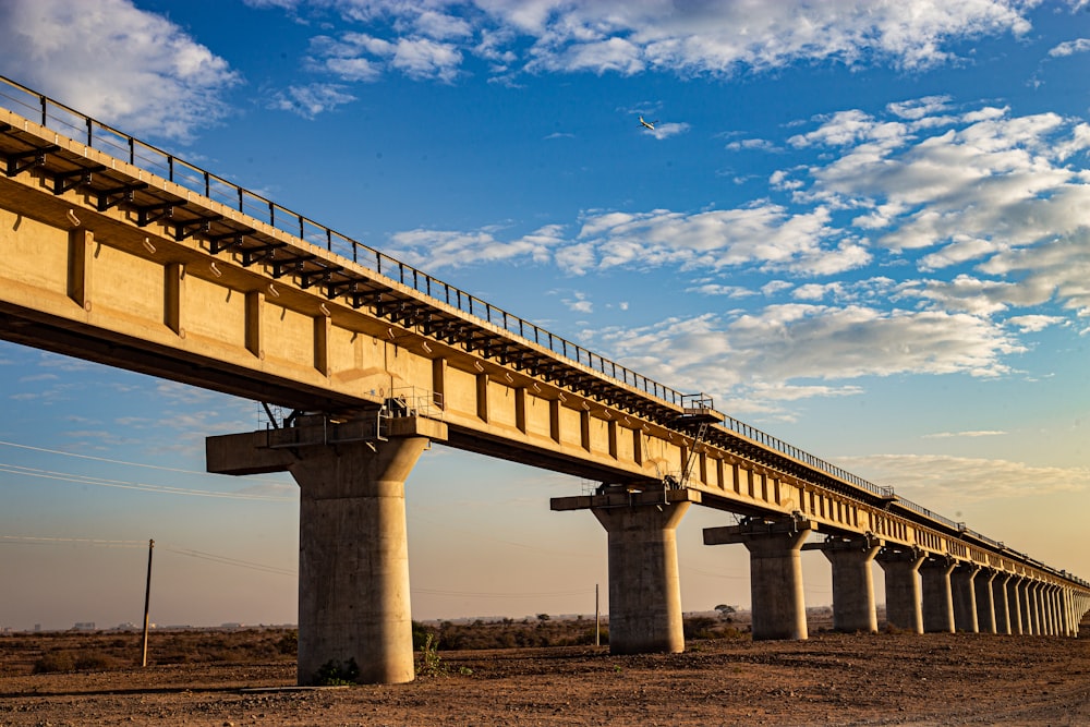 a large bridge over a dirt field under a blue sky