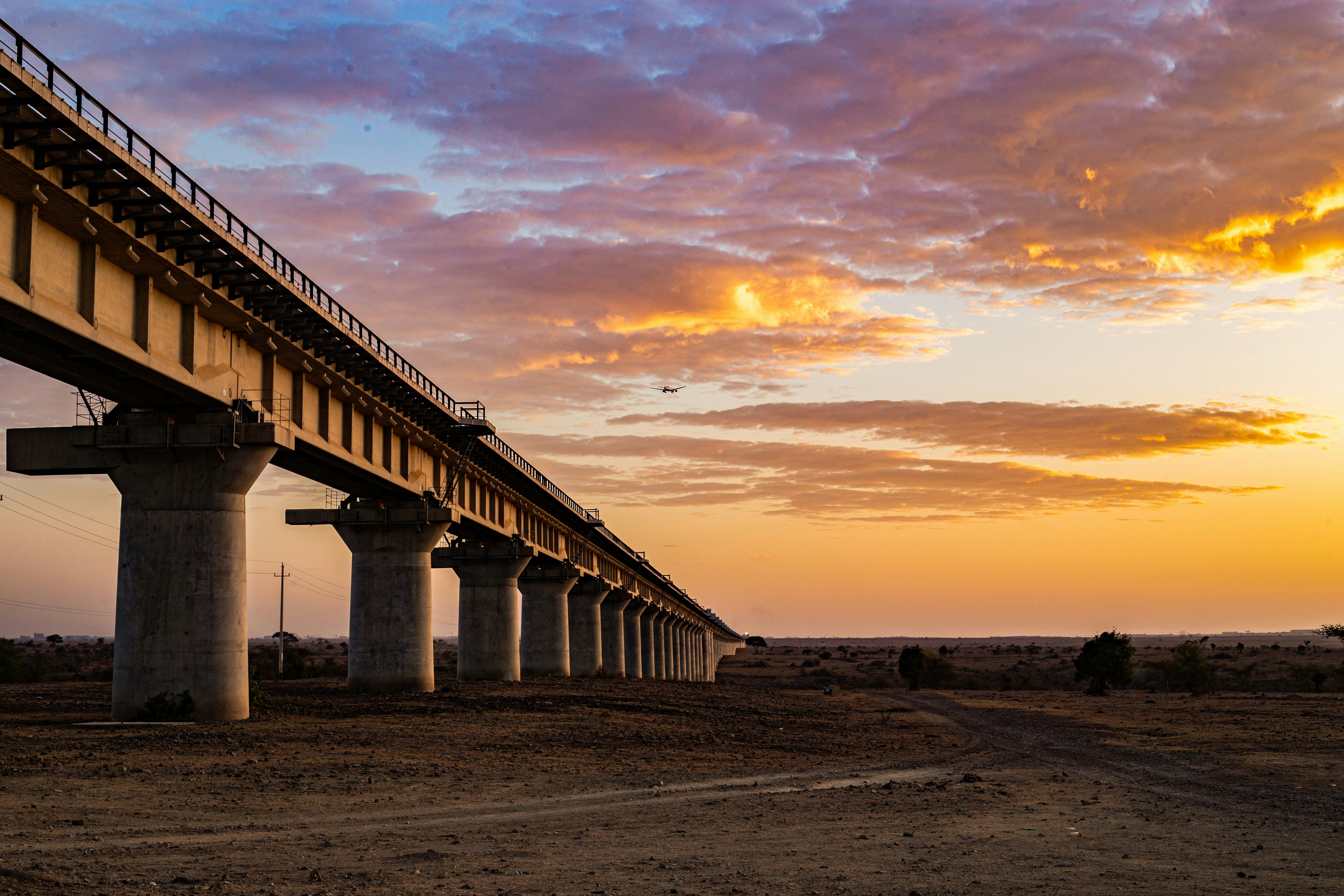 Le soleil se couche derrière un pont au-dessus d’un chemin de terre