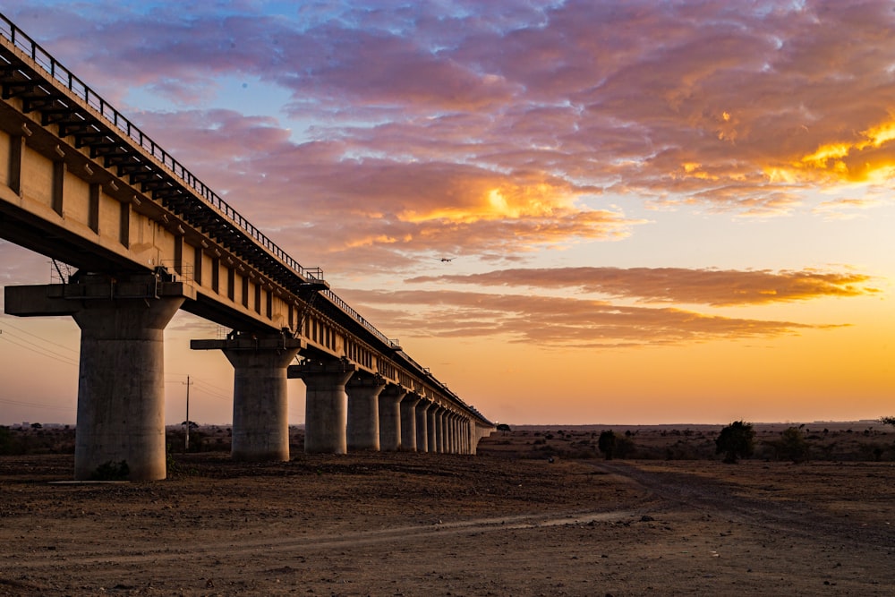 the sun is setting behind a bridge over a dirt road