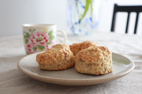 A steaming cup of coffee beside a plate of homemade scones on a rustic table.