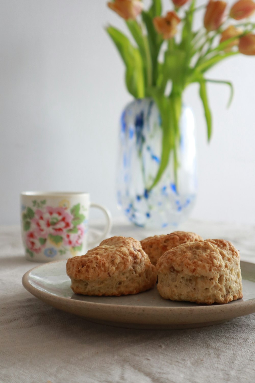 two biscuits on a plate next to a vase of flowers