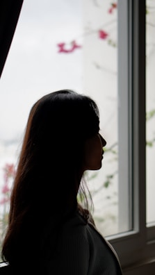 A soft pastel illustration of a woman journaling her feelings by a window with rose curtains.