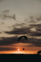 Sunset casting golden light on a paraglider gliding smoothly over winding mountain trails.