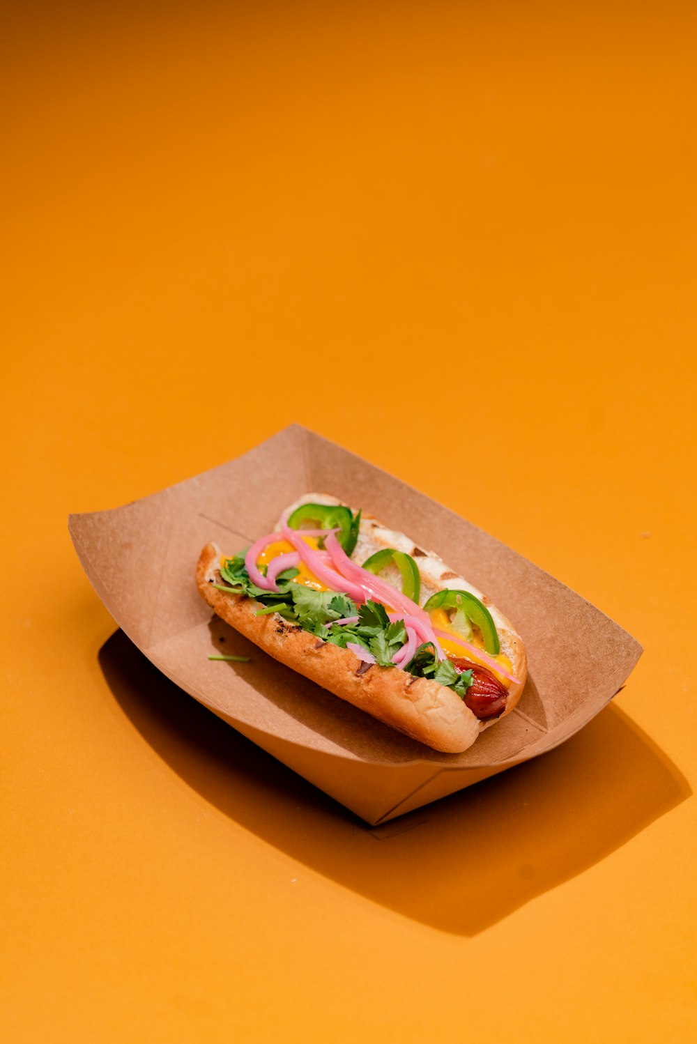 a hot dog in a paper container on a yellow surface