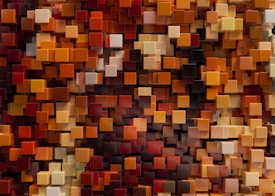 A densely packed arrangement of 3D cubes in various shades of orange, red, brown, and beige, creating a rich, textured mosaic.