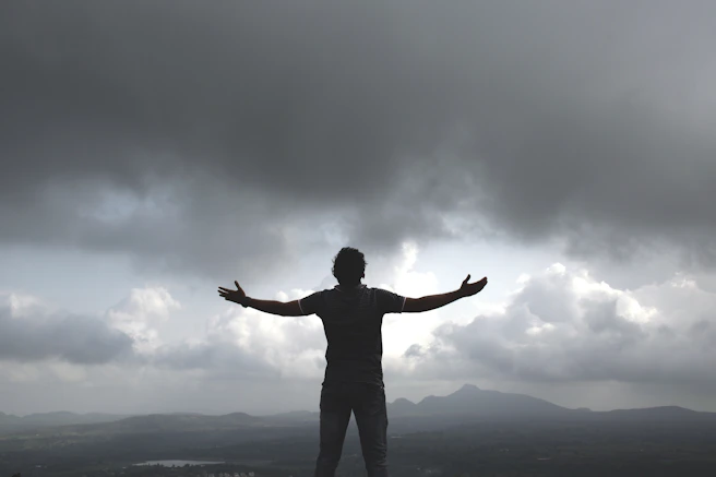 a man standing on top of a hill under a cloudy sky