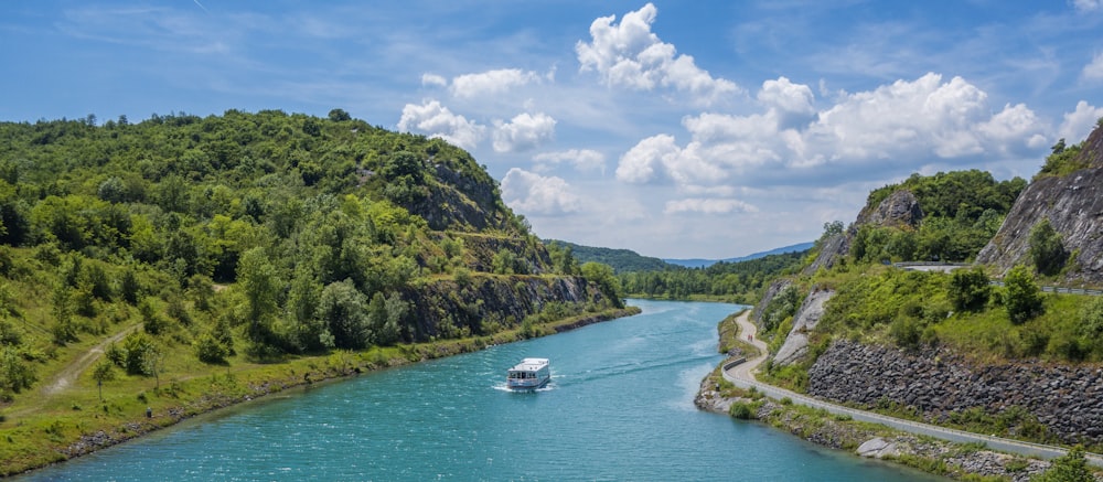 a boat traveling down a river next to a lush green hillside