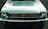 A front view of a vintage Ford Mustang with a teal color, featuring a distinctive grille and round headlights. The classic Mustang logo is prominently displayed at the center of the grille.