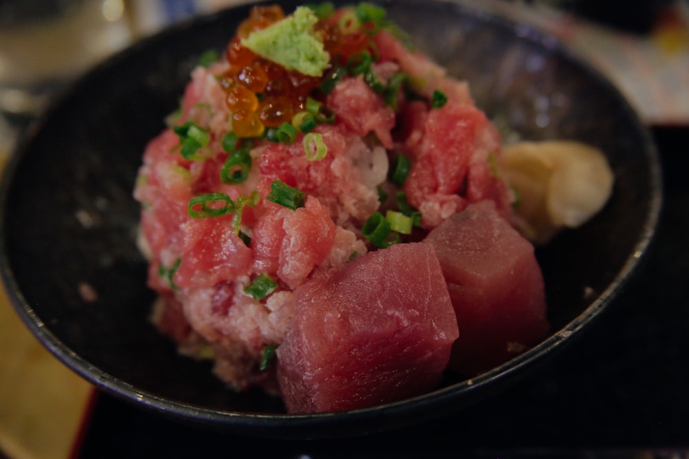 a black bowl filled with meat and vegetables