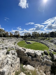 a grassy field surrounded by rocks under a blue sky