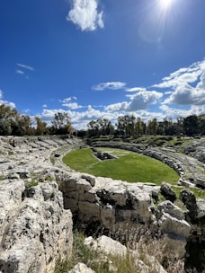 a grassy field surrounded by rocks under a blue sky