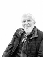 A middle-aged man with glasses and bald head wearing a yellow chicken-patterned pajama smiling gently.