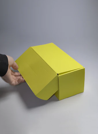 Close-up of hands holding a bright, neatly folded packaging box with a smooth finish.