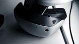 A close-up view of a virtual reality headset featuring a sleek design with a white and black color scheme. The image highlights details such as adjustment dials and a camera-like sensor on the device's exterior.