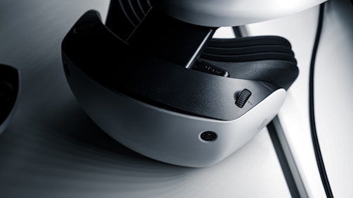 A close-up view of a virtual reality headset featuring a sleek design with a white and black color scheme. The image highlights details such as adjustment dials and a camera-like sensor on the device's exterior.