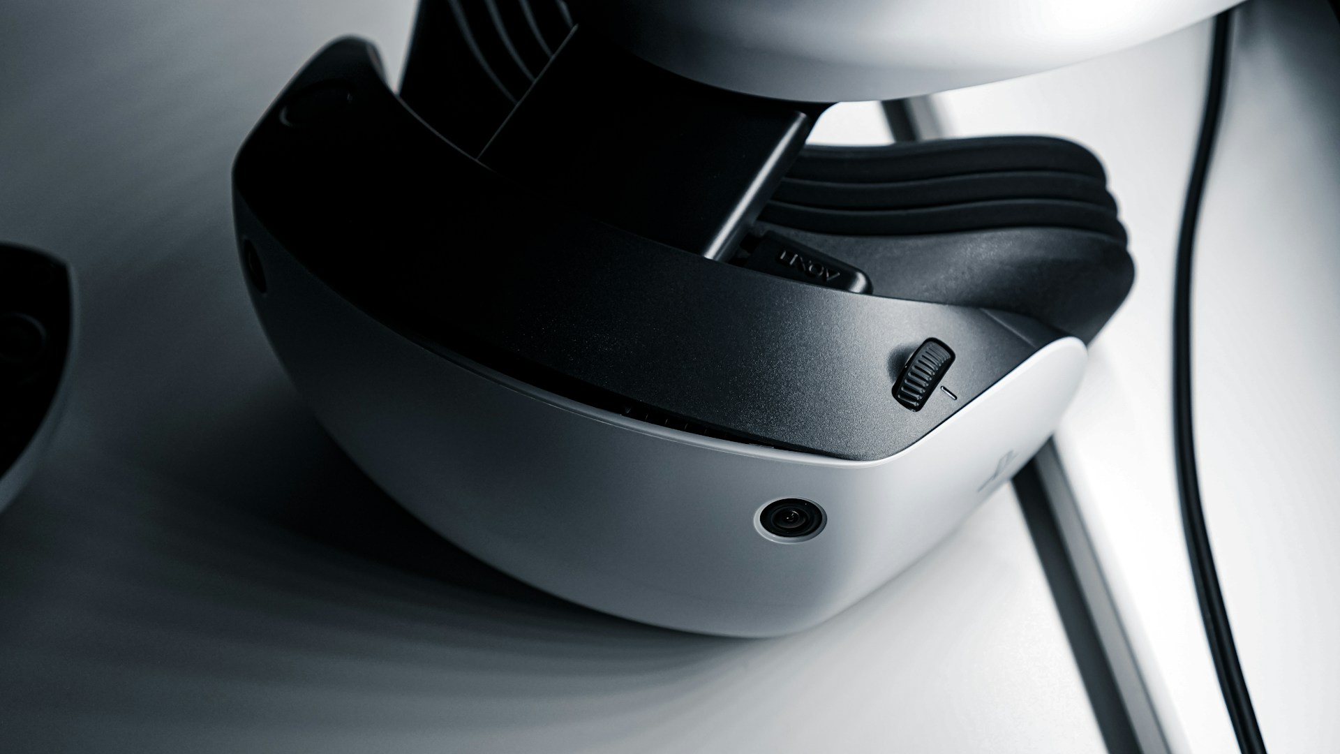 A close-up view of a virtual reality headset featuring a sleek design with a white and black color scheme. The image highlights details such as adjustment dials and a camera-like sensor on the device's exterior.