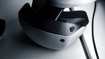 A close-up view of a virtual reality headset featuring a sleek design with a white and black color scheme. The image highlights details such as adjustment dials and a camera-like sensor on the device's exterior.