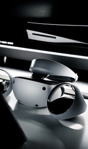 A sleek and modern virtual reality headset and controllers placed on a reflective surface. The lighting is dim, creating a dramatic and futuristic ambiance.