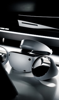A sleek and modern virtual reality headset and controllers placed on a reflective surface. The lighting is dim, creating a dramatic and futuristic ambiance.