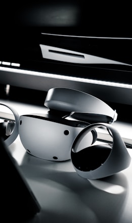 A sleek and modern virtual reality headset and controllers placed on a reflective surface. The lighting is dim, creating a dramatic and futuristic ambiance.