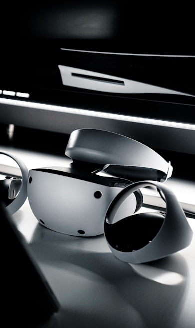 A sleek and modern virtual reality headset and controllers placed on a reflective surface. The lighting is dim, creating a dramatic and futuristic ambiance.