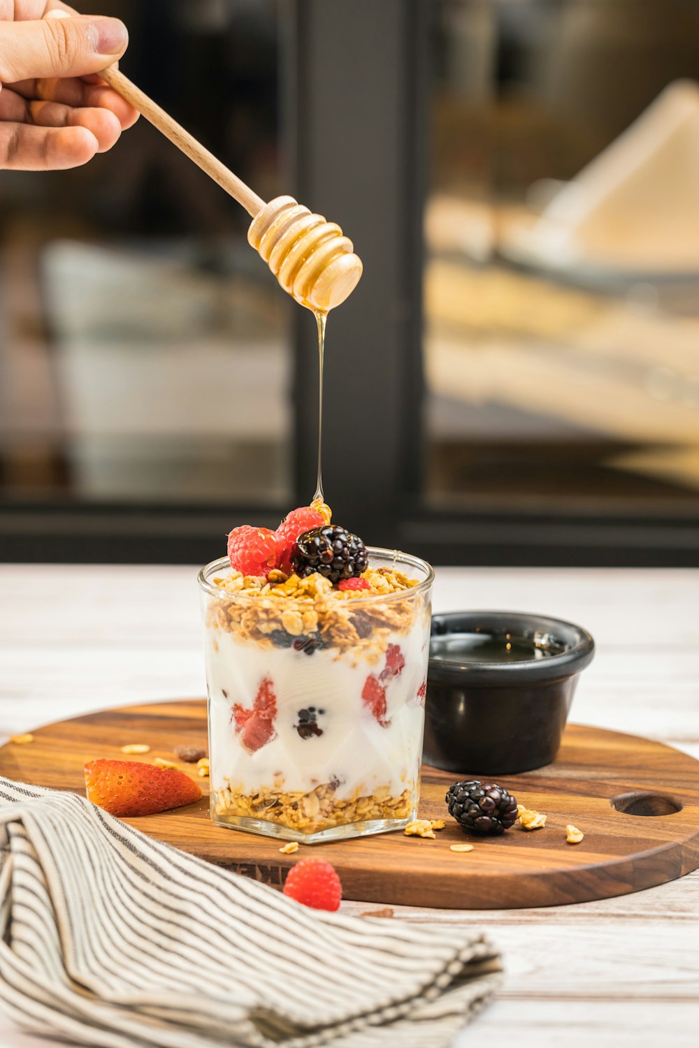 a person holding a wooden spoon over a glass of yogurt