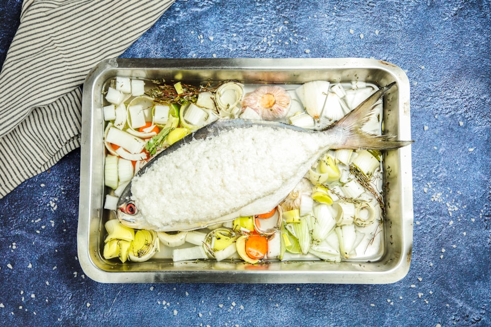 a fish in a pan with vegetables on a blue towel