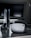 A sleek virtual reality headset sits on a reflective surface beside a gaming console and its controller. The background features a large dark monitor screen, creating a modern and futuristic setting. The lighting is subdued, highlighting the glossy surfaces of the electronic devices.