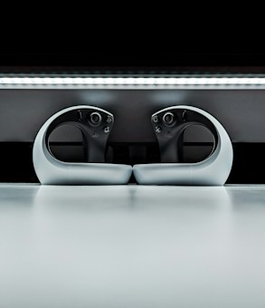 Two sleek, modern gaming controllers with an ergonomic design, placed symmetrically on a reflective surface. The background features a sleek horizontal light strip, enhancing the futuristic appearance.