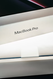 A close-up view of a MacBook Pro box, showcasing the sleek packaging design, primarily in white, with the words 'MacBook Pro' prominently displayed on the side. The image captures the clean lines and minimalistic style typical of Apple product packaging.