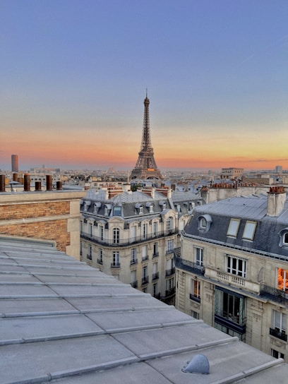 A golden sunset casting warm light over the Eiffel Tower, with Parisian rooftops in the foreground.