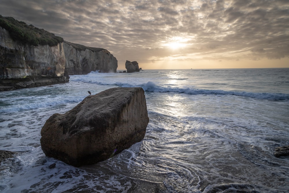 a large rock sitting on top of a beach next to the ocean