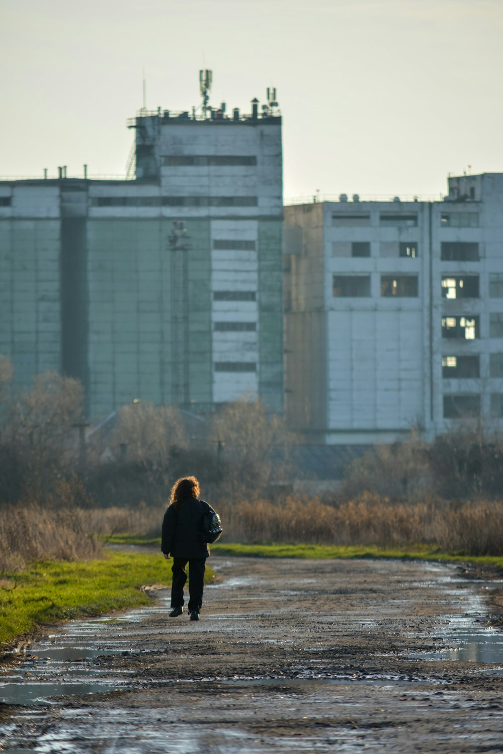 a person walking down a dirt road in front of a building