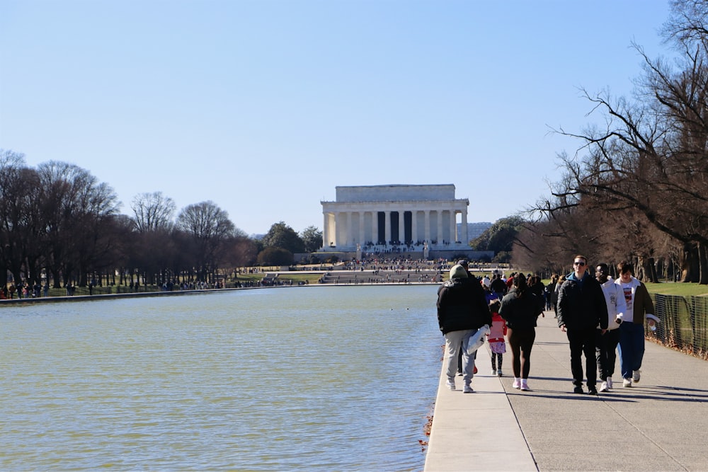 a group of people walking down a sidewalk next to a body of water